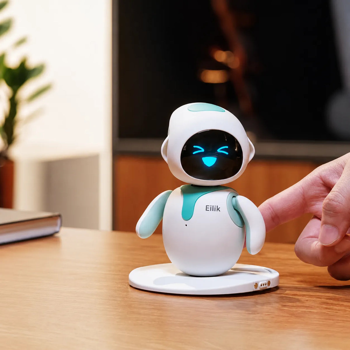 Ein Eilik-Roboter auf einem Schreibtisch, eine Hand streckt sich von rechts nach ihm aus.